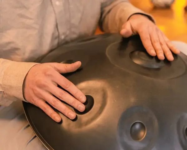 Dłonie grają na instrumencie typu hang drum, tworząc kojące dźwięki.