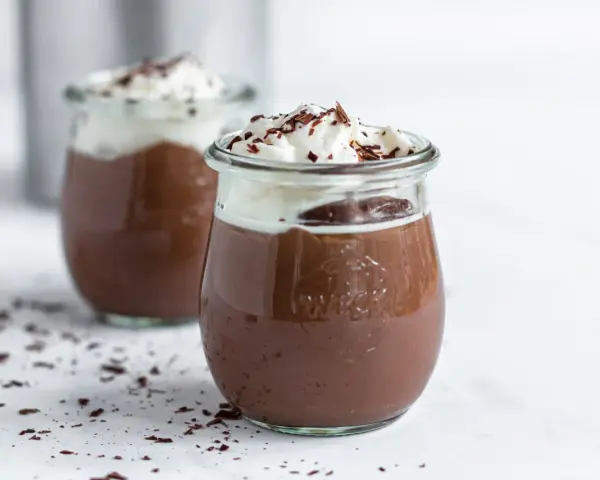 Zwei Gläser mit cremigem omas schokoladenpudding, gekrönt mit Schlagsahne und Schokostreuseln.