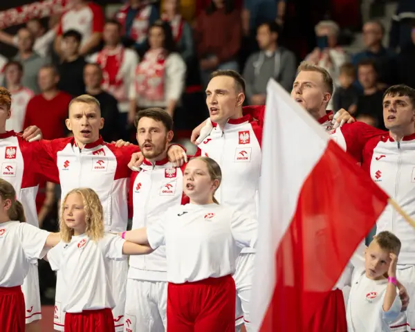 Polska drużyna piłki ręcznej z flagą narodową. Młodzi zawodnicy i dzieci w strojach biało-czerwonych.