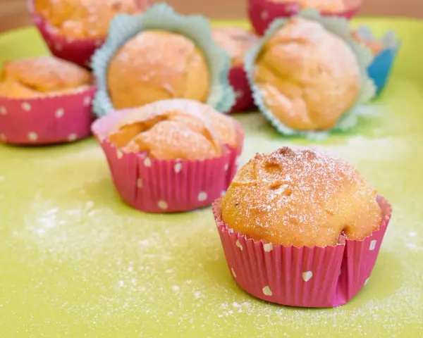 Leckere Muffins ohne Ei, bestäubt mit Puderzucker, in bunten Papierförmchen auf einer hellgrünen Platte.