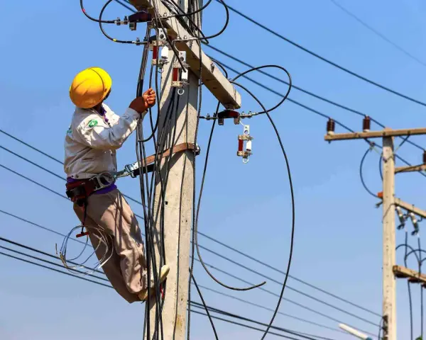 Elektryk w żółtym kasku pracuje na słupie energetycznym, podłączając przewody. Zastanawiasz się, ile kosztuje przyłącze elektryczne?