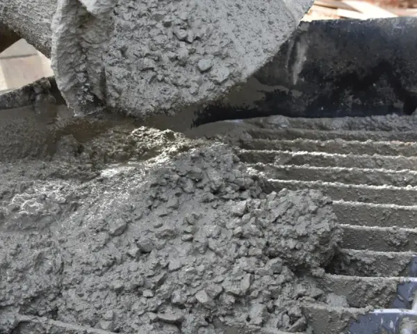 Świeży beton z kruszywem, idealny jako jaki beton pod obrzeża, wylewany z maszyny na ruszt.