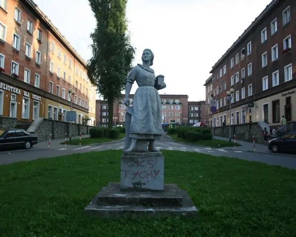 Pomnik w stylu socrealizmu na tle bloków mieszkalnych.