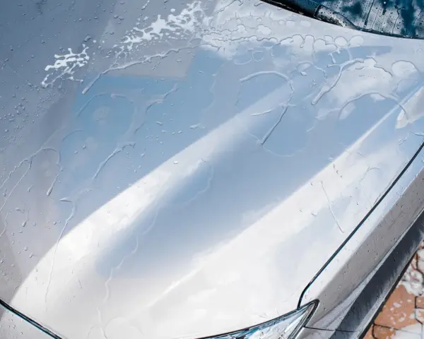 Krople wody i piany na masce srebrnego auta. Czy po woskowaniu płukać auto? Tak, aby uzyskać idealny połysk.