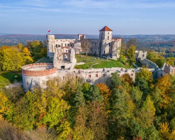 Ruiny zamku na Szlaku Orlich Gniazd, otoczone jesiennym lasem. Majestatyczne mury i wieże górują nad okolicą.