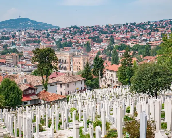 Widok na cmentarz z białymi nagrobkami i panoramę Sarajewa. Warto zobaczyć to miejsce, by poczuć historię miasta.