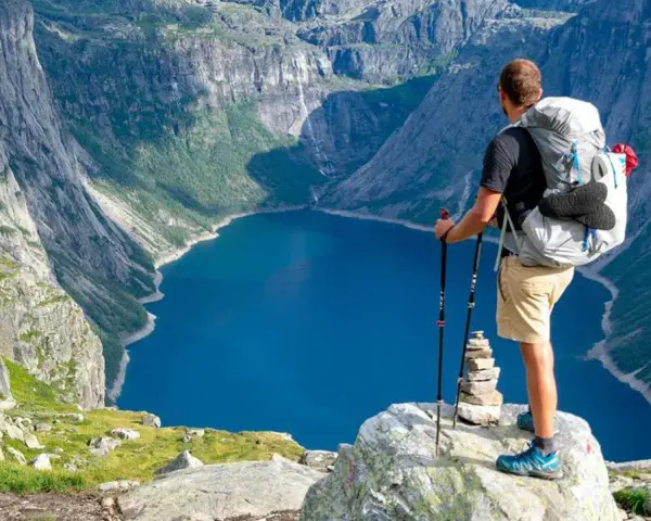 Un escursionista con zaino e bastoncini ammira un lago blu intenso circondato da montagne imponenti. Un'avventura di trekking montagna indimenticabile.