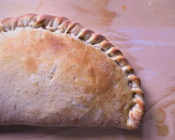 Złocisty calzone, pieczony na drewnianym tle, z charakterystycznym, zaplecionym brzegiem. Idealny na szybki posiłek.