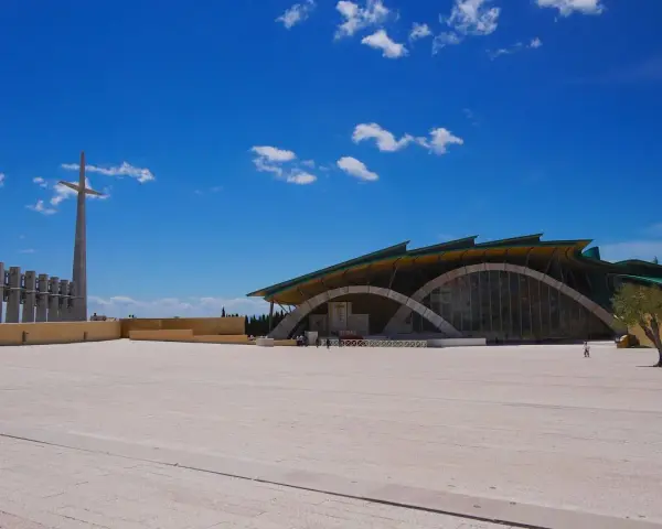 The modern church of San Giovanni Rotondo Padre Pio stands under a bright blue sky, with a tall cross and bell tower in the distance.