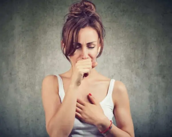 Mujer tosiendo y con dolor de cabeza, quizás por vapear.