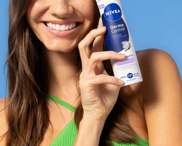 Uśmiechnięta kobieta trzymająca dezodorant Nivea Derma Control na tle niebieskiego tła.