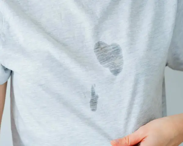 Gros plan sur une tache d'huile sur un vêtement gris clair. La tache est sombre et semble avoir pénétré le tissu.