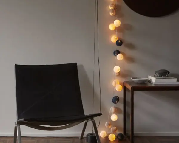 En svart läderfåtölj står bredvid ett bord med böcker och en skål. En ljusslinga med runda ljus ger en mysig inredning med ljusslingor.