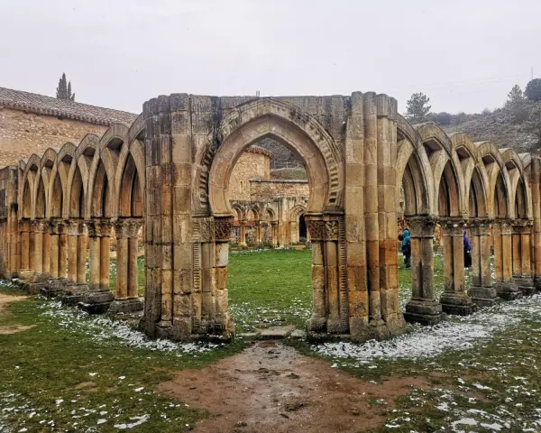 Ruinas de un claustro con arcos de piedra, evocando el nacimiento del Duero. Nieve ligera cubre el césped.
