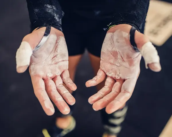 Mains de sportif couvertes de magnésie, prêtes à saisir la barre. Une corne sur la main témoigne des efforts.