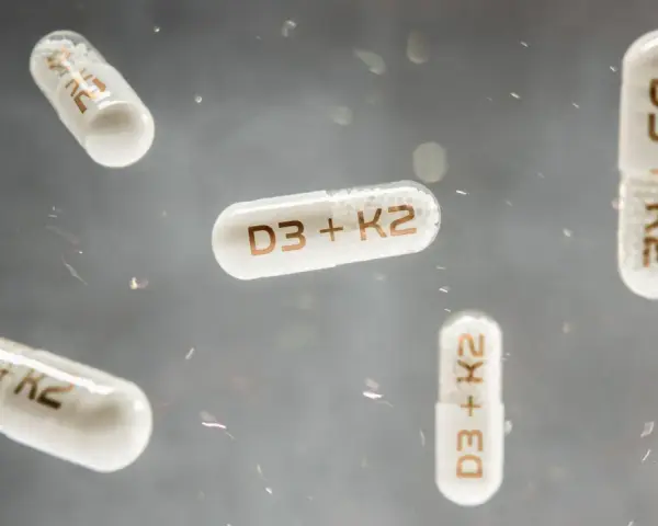 Flera kapslar med texten "D3 + K2" svävar i luften. Dessa kapslar kan vara ett komplement till din k vitamin mat.