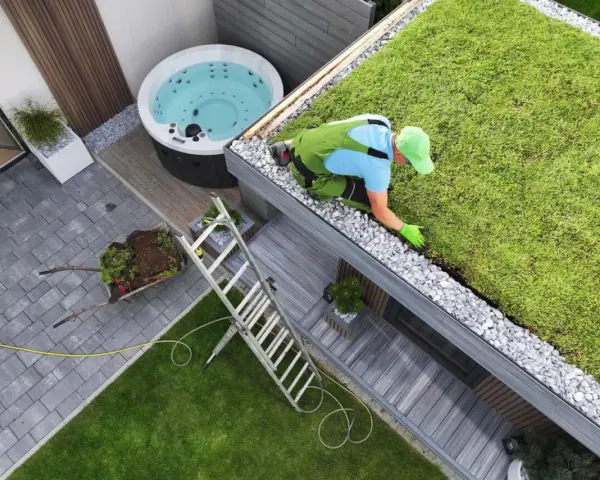 Pracownik pielęgnuje zielony dach, przykład **powierzchni biologicznie czynnej definicji**. Obok jacuzzi i taras.