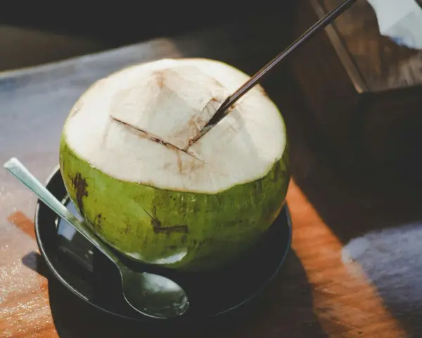 Une noix de coco verte ouverte avec une paille, prête à déguster. Découvrez les nombreux bienfaits de l'eau de coco pour une hydratation naturelle.