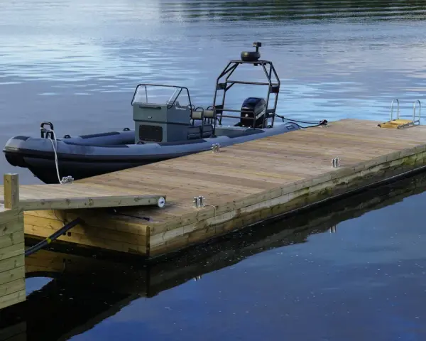 En grå RIB-båt ligger förtöjd vid en nybyggd flytbrygga i trä. Perfekt för att bygga flytbrygga och njuta av vattnet.