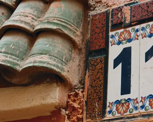 Numerologiczna 11 mężczyzna, jak liczba 11 na ozdobnej tabliczce obok zielonych dachówek, symbolizuje intuicję i duchowość.