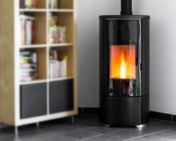 Stufa a pellet moderna in camera da letto, con fiamme vive che illuminano l'ambiente. Accanto, una libreria in legno con libri.