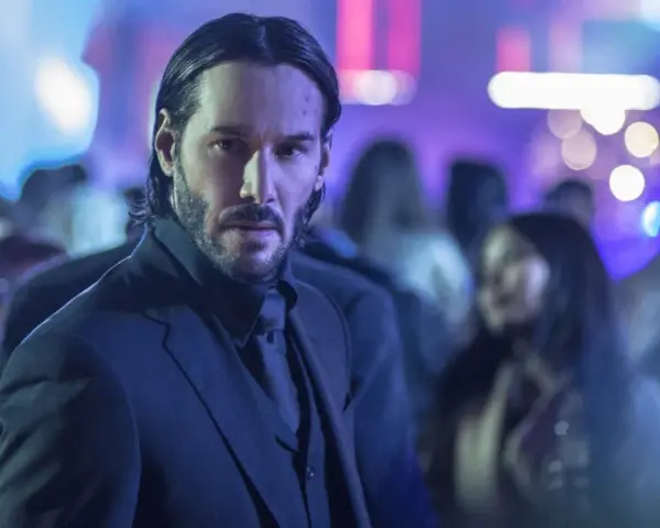 Keanu Reeves w garniturze, w tle rozmyte światła i tłum. Ikona kina akcji, znana z filmów takich jak John Wick.