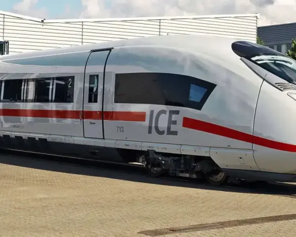 Biały pociąg ICE 5 z czerwonym pasem stoi na torach przed budynkiem.