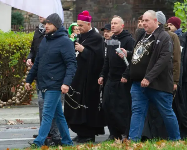 Grupa mężczyzn, w tym biskup, idzie ulicą. Niektórzy niosą różańce, jak rycerze Maryi.