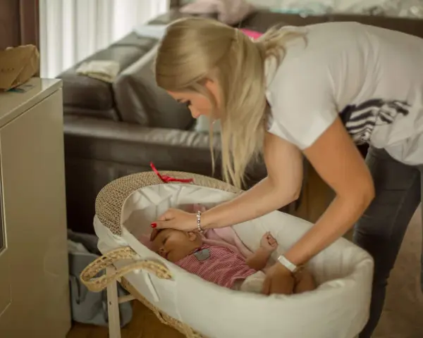 Mama delikatnie kładzie śpiące dziecko do kosza. To początek nauki samodzielnego zasypiania bez płaczu.