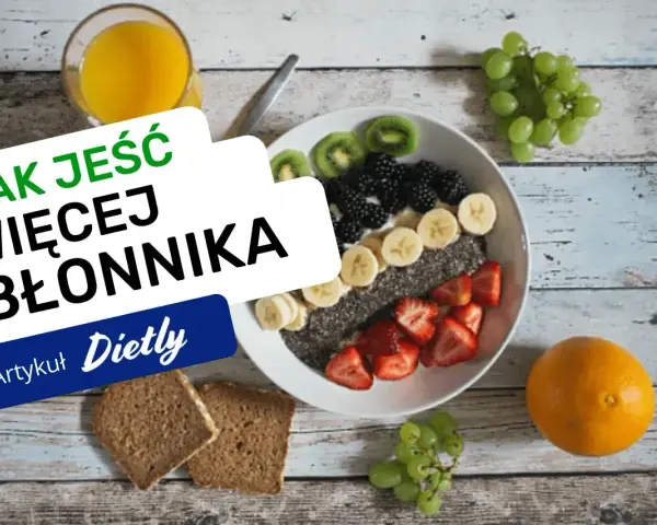 Pyszna owsianka z owocami i nasionami chia, idealna na śniadanie, które ma duzo blonnika. Obok szklanka soku i kromki chleba.