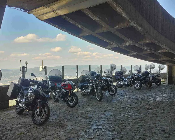 Motocykle pod betonowym zadaszeniem, z widokiem na krajobraz przypominający szwajcarskie Czechy.