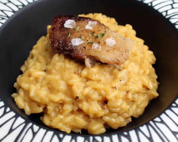 Cremoso risotto a la milanesa, coronado con un trozo crujiente y salpicado de sal marina y hierbas.