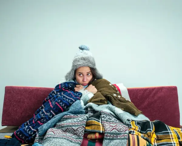 Kobieta w ciąży, otulona wieloma swetrami i kocami, czuje silne uczucie zimna.
