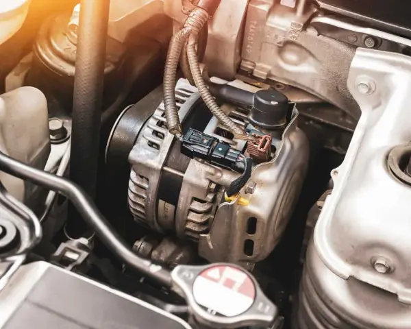 Zbliżenie na alternator samochodowy w komorze silnika, z widocznymi przewodami i elementami mechanicznymi.