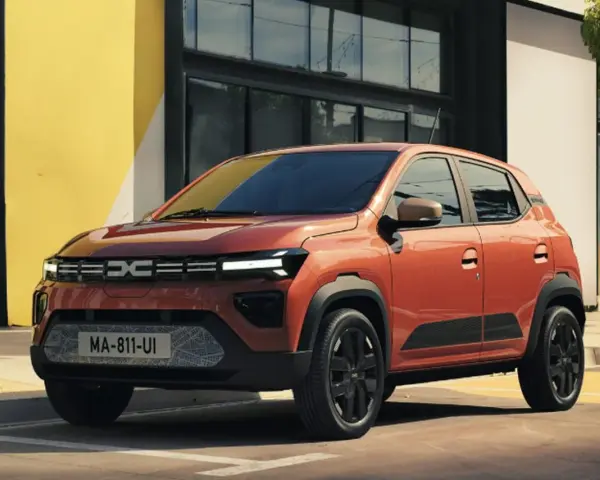 Pomarańczowy Dacia Spring stoi przed budynkiem z żółtą ścianą.