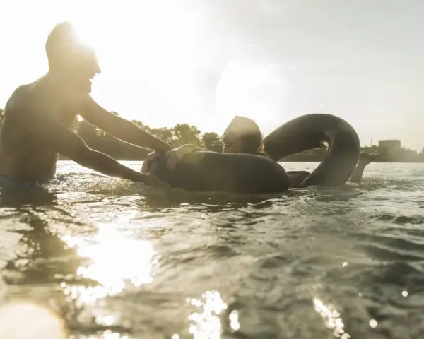 Ein Mann hilft einer Frau mit einem Schwimmring im Wasser. Ein sonniger Tag am Badesee Braunschweig.