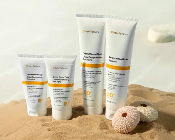 Cuatro tubos de crema solar biodegradable de Thader Pharma en la arena, con dos erizos de mar.