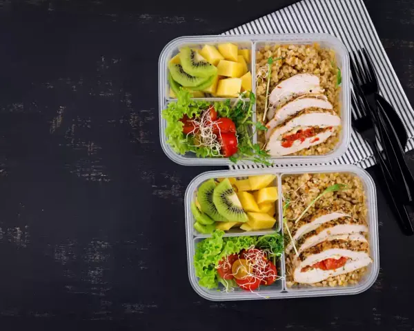 Dwa pudełka na lunch do pracy: kurczak faszerowany, kasza, sałatka z pomidorkami i kiełkami, kiwi i mango.
