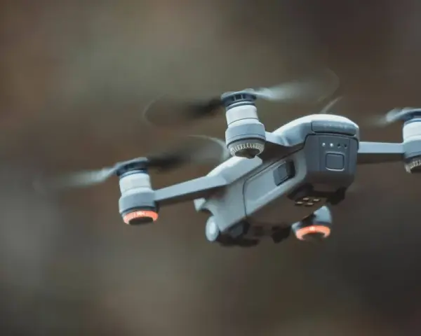 A drone hovers mid-air, its propellers a blur. Red anti-collision lights glow on its arms, ensuring safe flight.