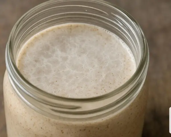 Ein Glas mit aktivem Sauerteig, bereit für die Zubereitung von Brot. Die kahmhefe zeigt sich in feinen Bläschen.