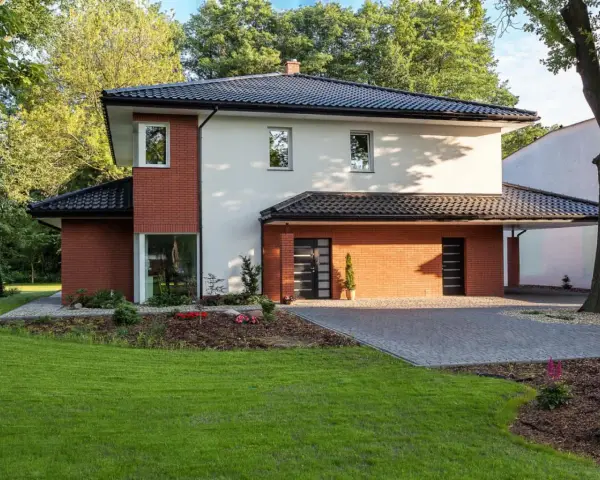 Nowoczesny dom z ceglanymi akcentami i eleganckim, czarnym dachem czterospadowym, otoczony zielenią.