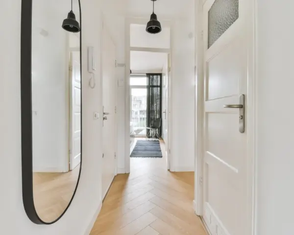 Un ampio specchio nel corridoio riflette le porte bianche e il pavimento in parquet.