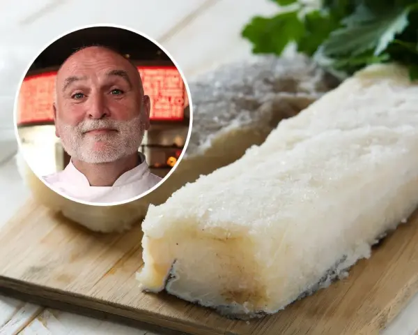 Chef sonriente junto a trozos de bacalao en salazón sobre tabla de madera.