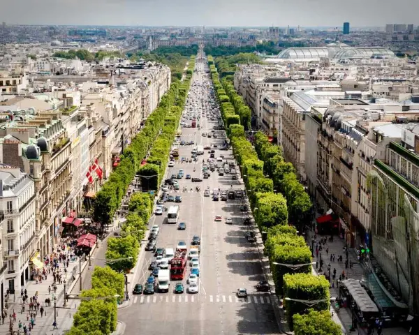 Vista aérea de la **Champs-Élysées** en París, con tráfico y peatones paseando entre los árboles y edificios.
