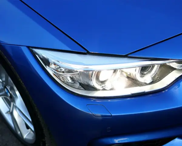 Blå BMW-strålkastare, redo för prewash. En del av en sportig bil med blanka fälgar.