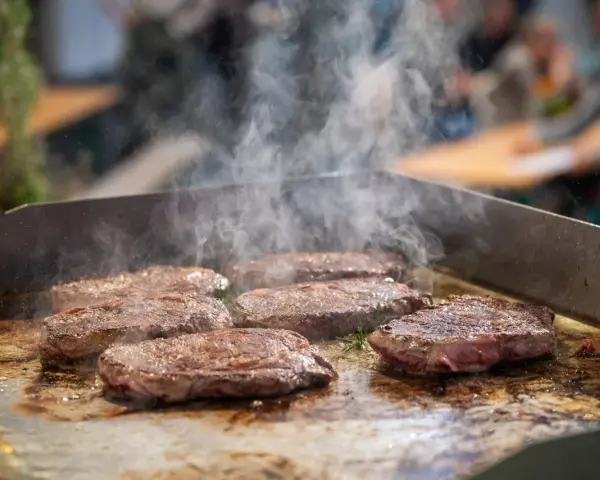 Mehrere saftige Rumpsteaks braten auf einer heißen Platte, Dampf steigt auf.