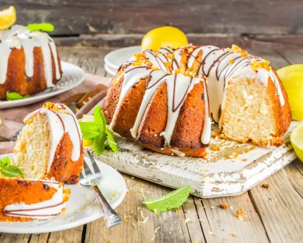 Najlepsza babka cytrynowa wilgotna na oleju, ozdobiona lukrem i skórką cytrynową, z kawałkami na talerzykach.
