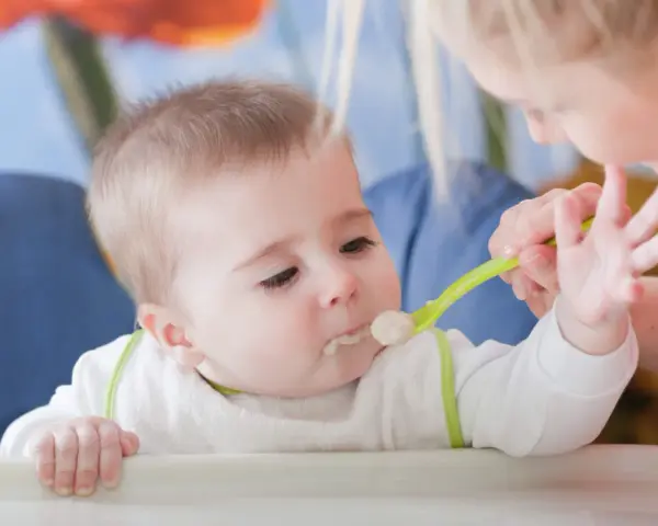 Mama karmi dziecko łyżeczką do karmienia niemowląt. Maluch z zaciekawieniem patrzy na jedzenie.