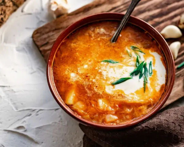 Un tazón de sopa de ajo con crema y cebolleta, acompañado de ajos y cebolletas.