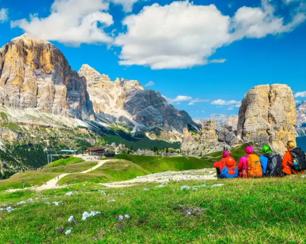 Quattro escursionisti ammirano un maestoso itinerario dolomiti, con cime imponenti e un rifugio alpino.